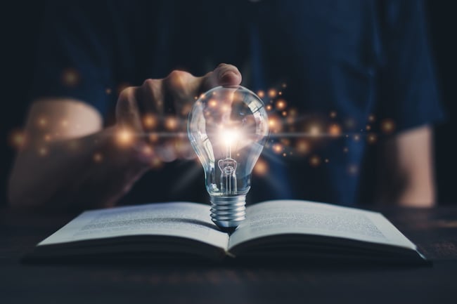 Finger on glowing lightbulb on top of book | Funnel Clarity