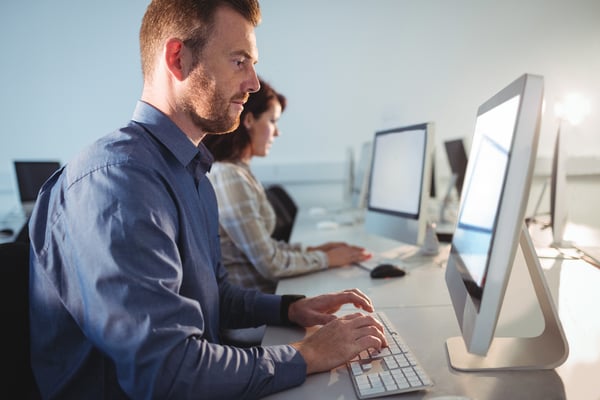 Business man at desk in office with colleagues also sitting at computers around him