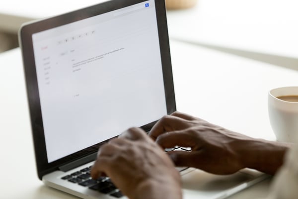 African-American man typing email on silver laptop