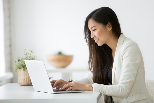 Young woman in suit typing emails on laptop in an office